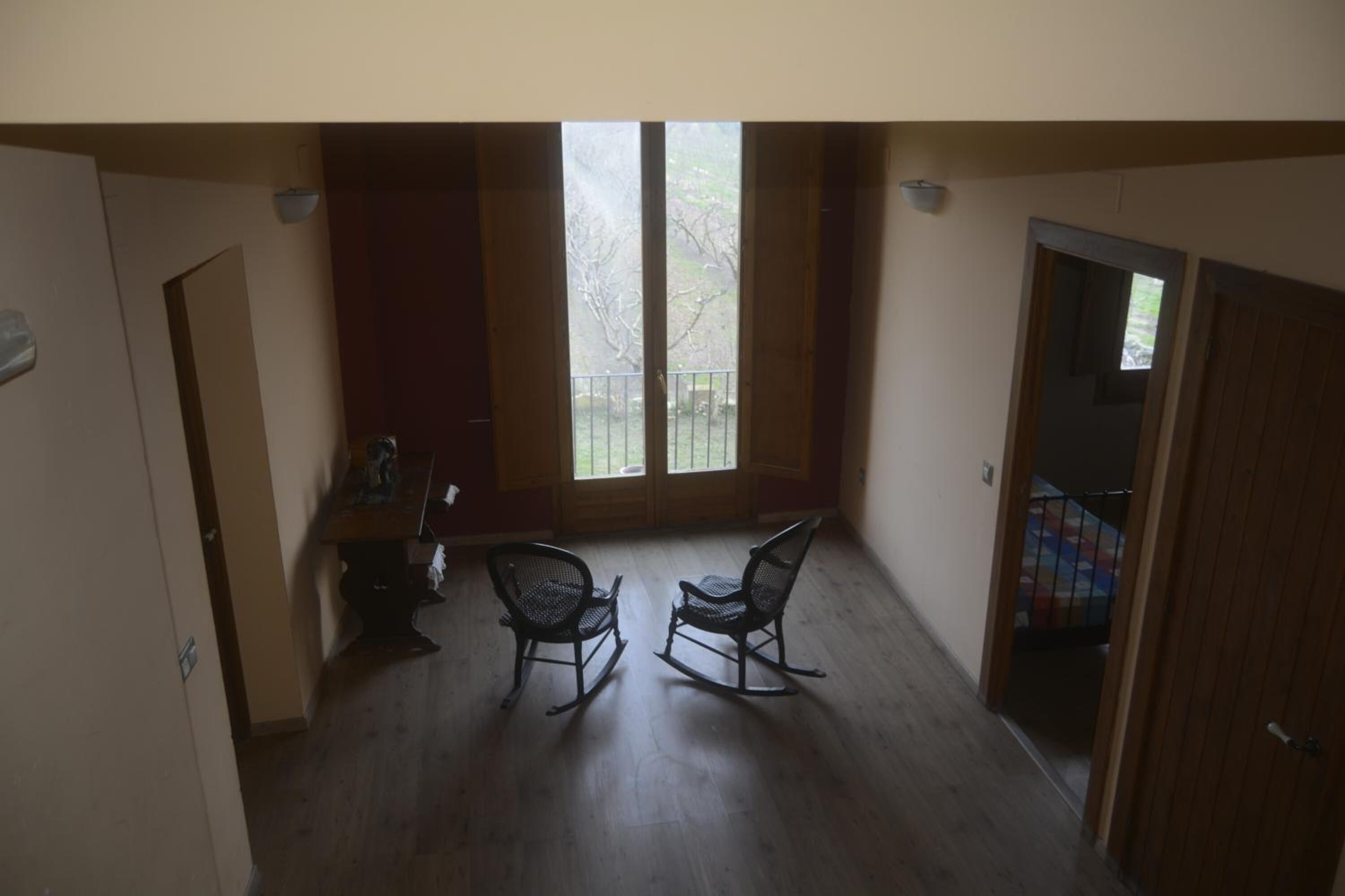 A room with two rocking chairs, a wooden floor, and a large window with a view of trees.
