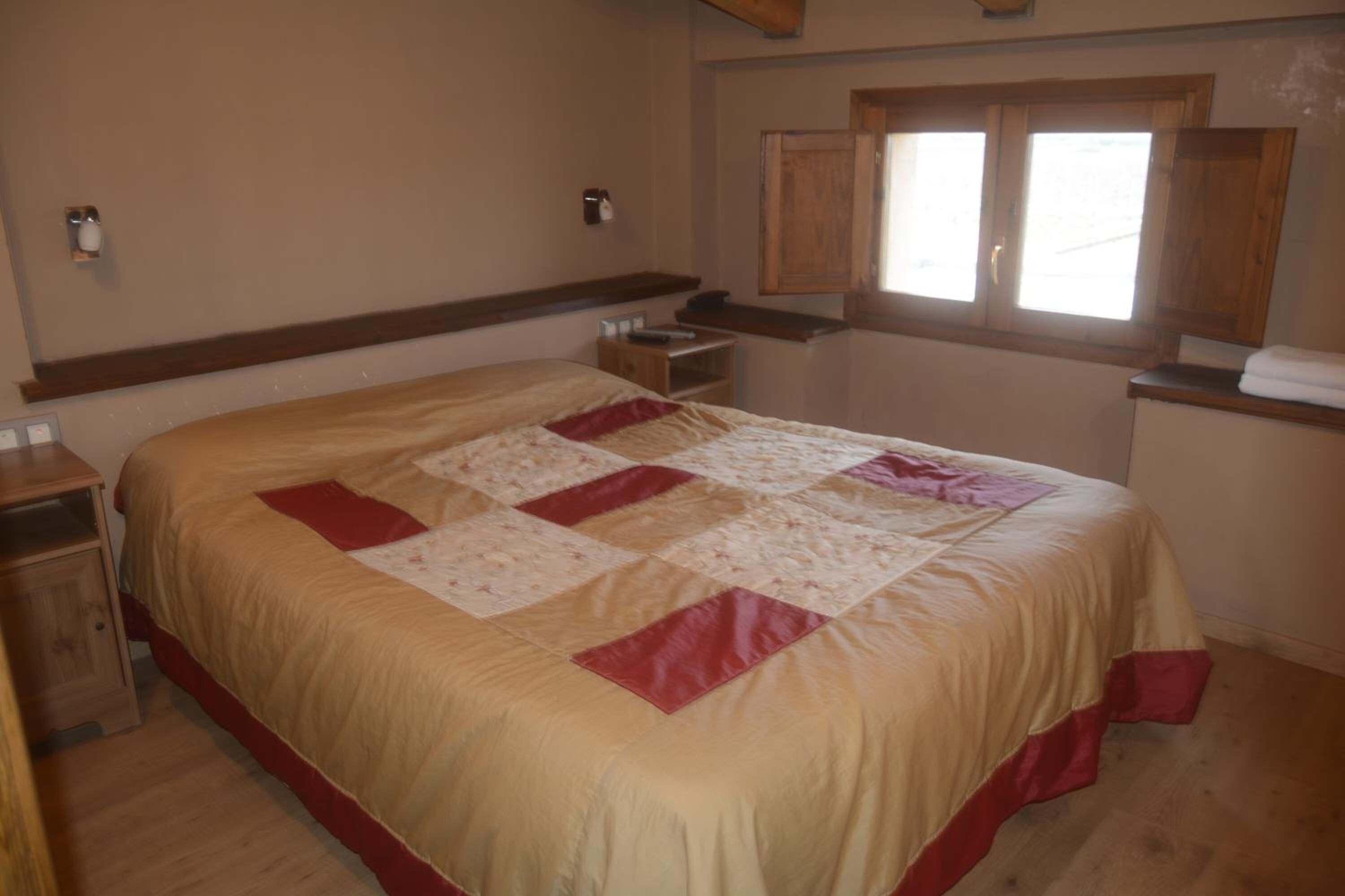 A bedroom with a large bed, wooden headboard, bedside tables, and a window with wooden shutters.