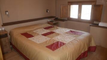 A bedroom with a large bed, wooden headboard, bedside tables, and a window with wooden shutters.