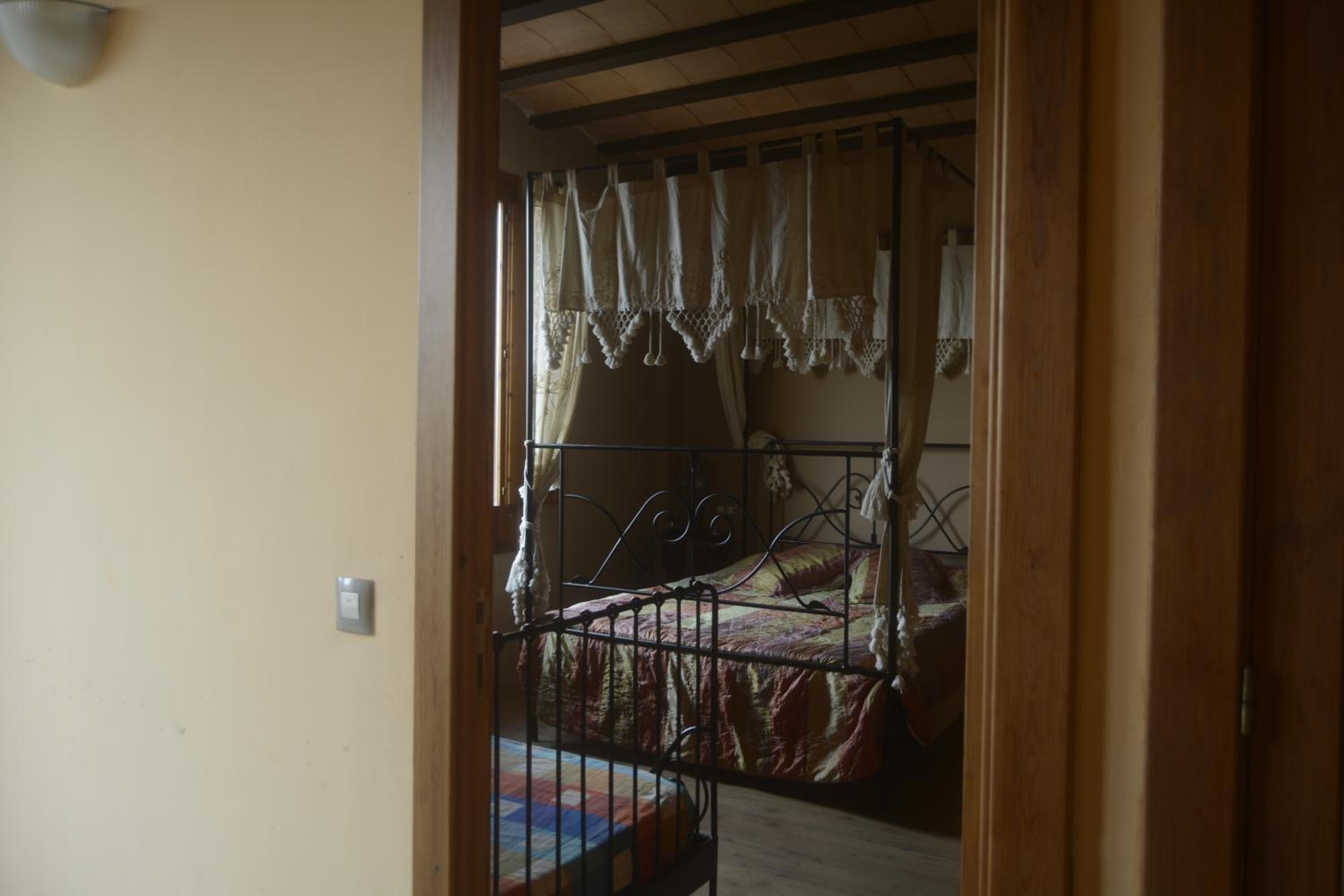 Un dormitorio con estructura de cama metálica, colcha acolchada y ventana con cortinas.