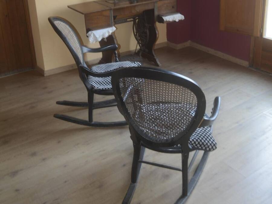 A room with a wooden dining table, two rocking chairs, a sewing machine, and a light fixture on the wall.
