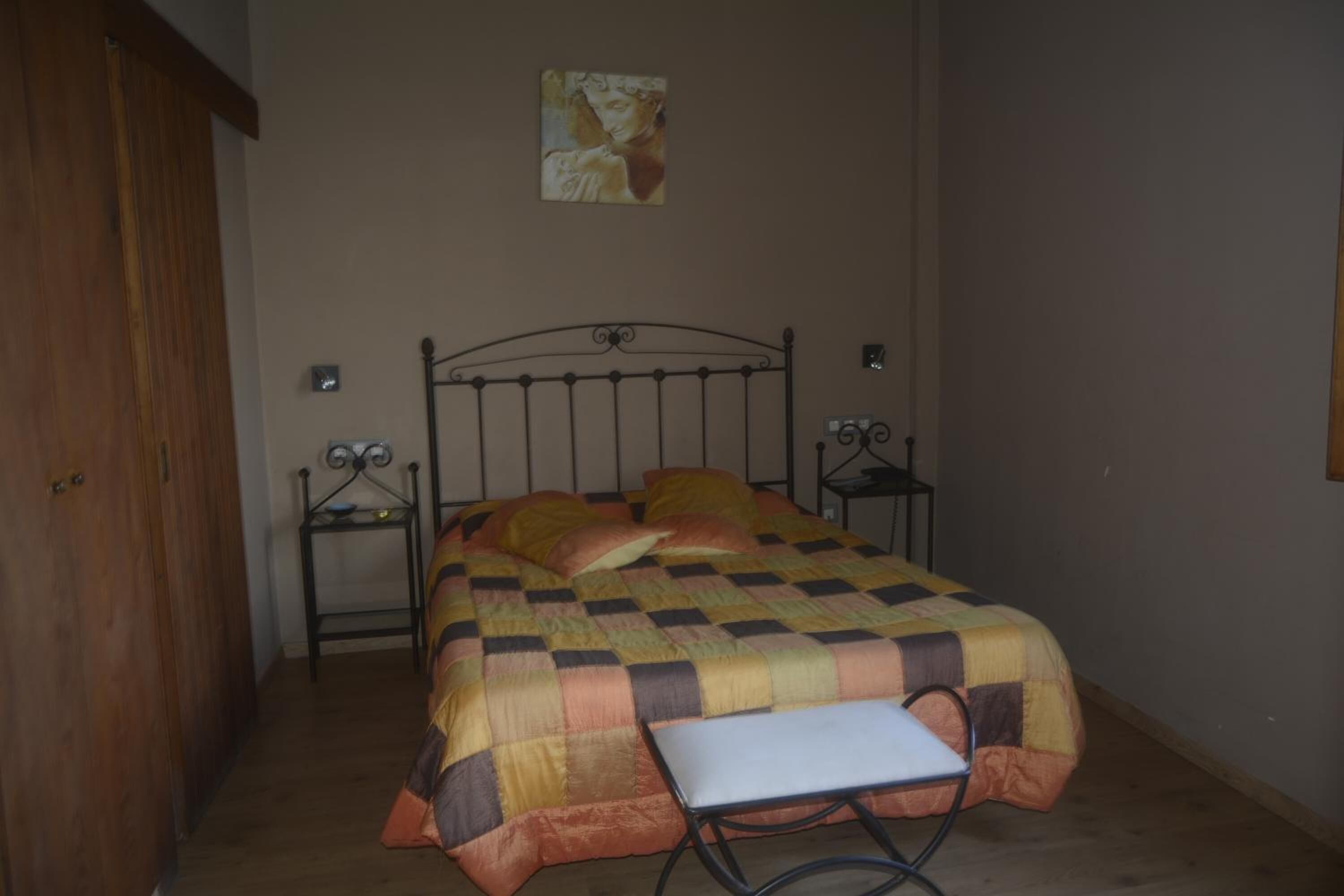 Un dormitorio con una cama, una mesita de noche, una silla y una obra de arte colgada en la pared.