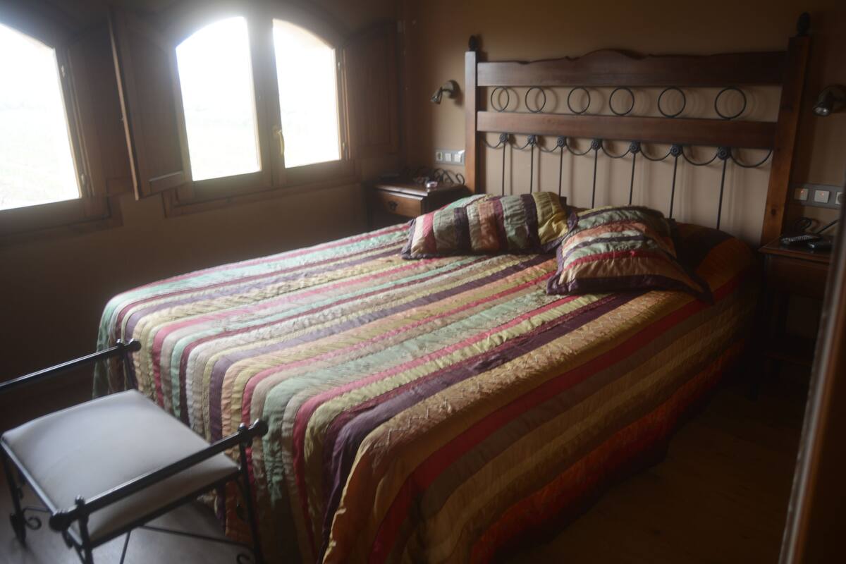 A bedroom with a large bed, a bedside table, a chair, and a window.