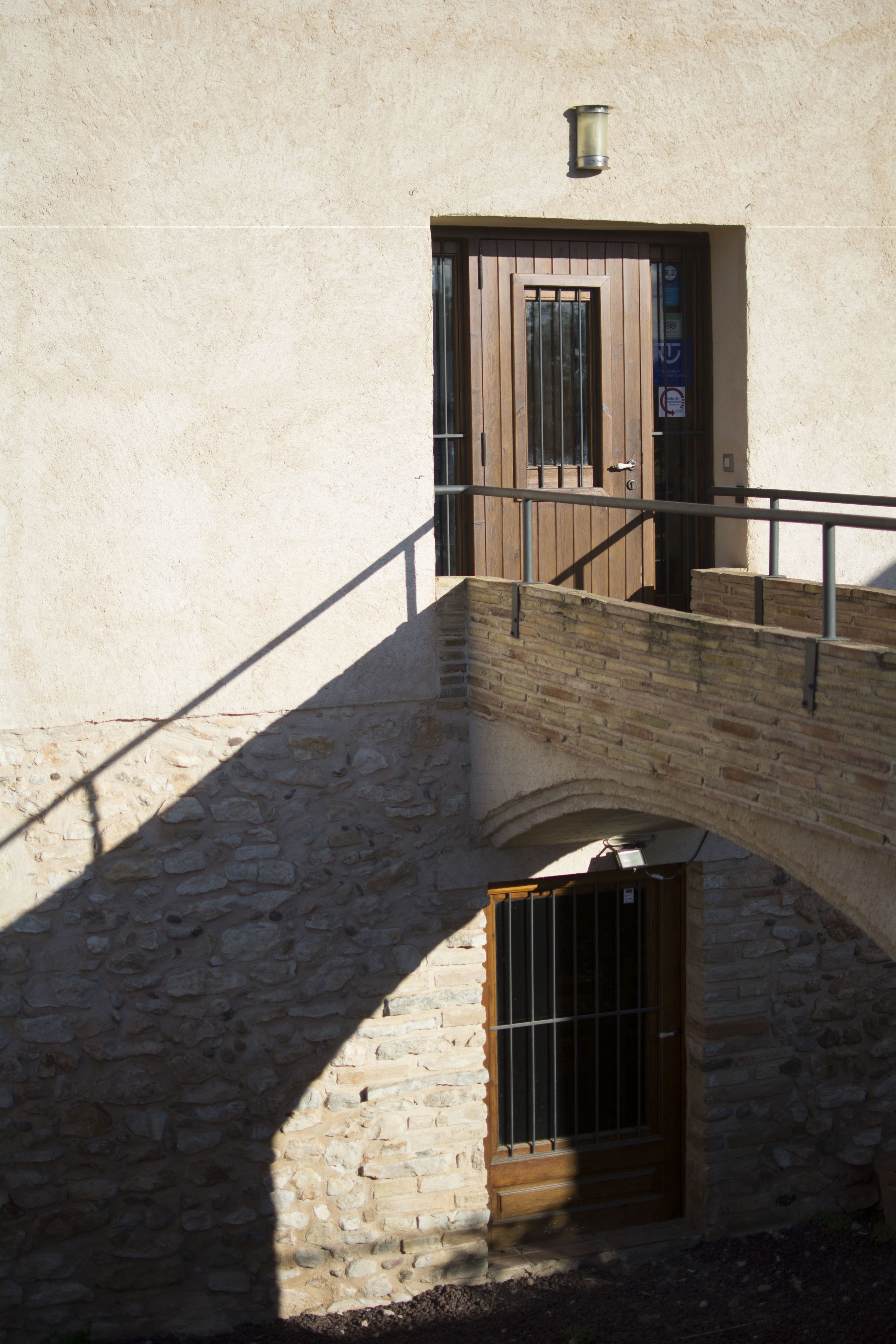 A stone staircase leading to a wooden door with a metal gate, set against a plain wall.