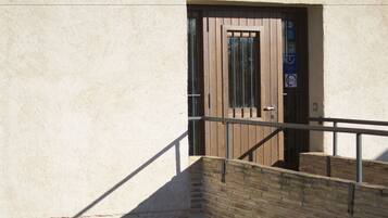 A stone staircase leading to a wooden door with a metal gate, set against a plain wall.