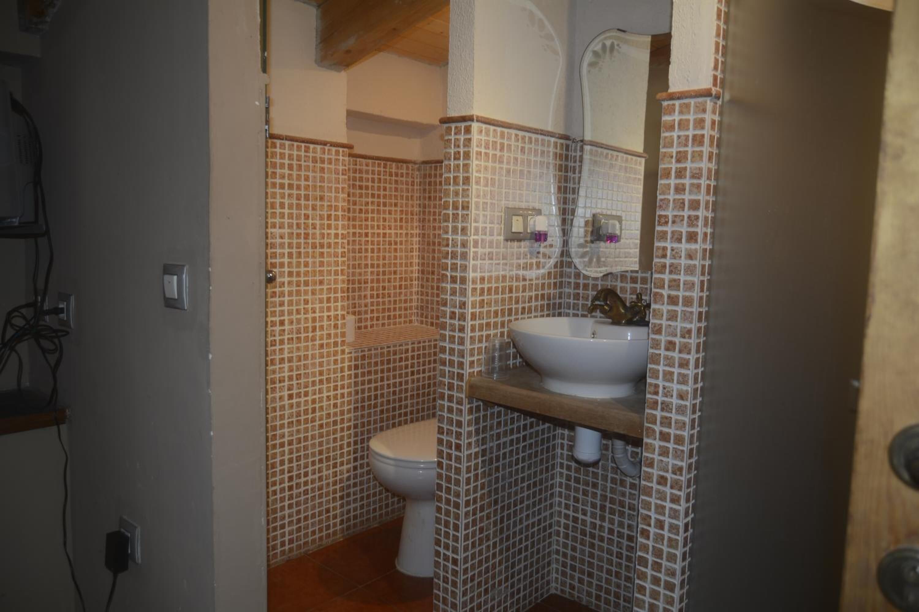 A bathroom with a tiled floor, a toilet, a sink, and a mirror.