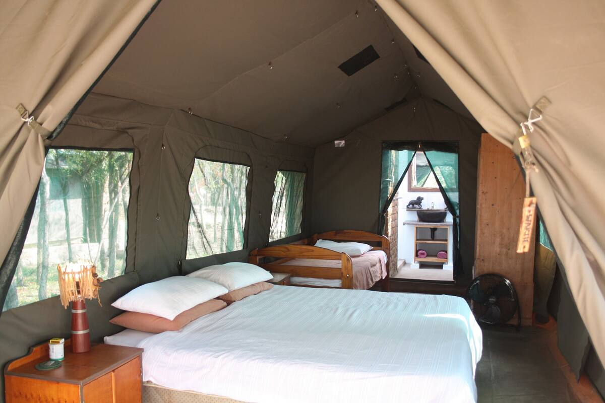 A tent with two beds, a small table, and a shelf with items.