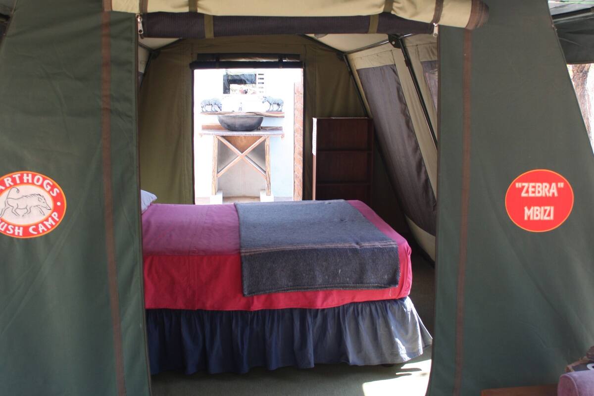 A tent with a bed, a chair, and a window.