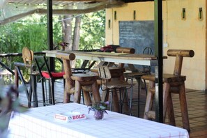 Un espace extérieur aménagé pour les repas, avec des tables et des chaises en bois rustique, un tableau noir servant de menu et une enseigne indiquant un restaurant nommé « BOLS ».