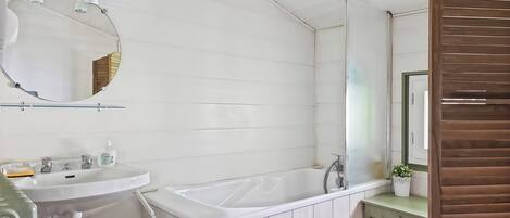 A bathroom with a white sink, a mirror, a bathtub, and a wooden panel wall.