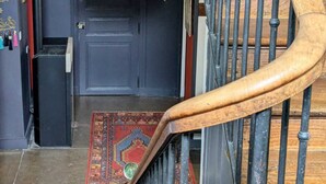 A wooden staircase leading to a dark blue door with a decorative handle and a small window. A colorful rug is placed on the floor in front of the door. - Villa Rhôna (Andancette)