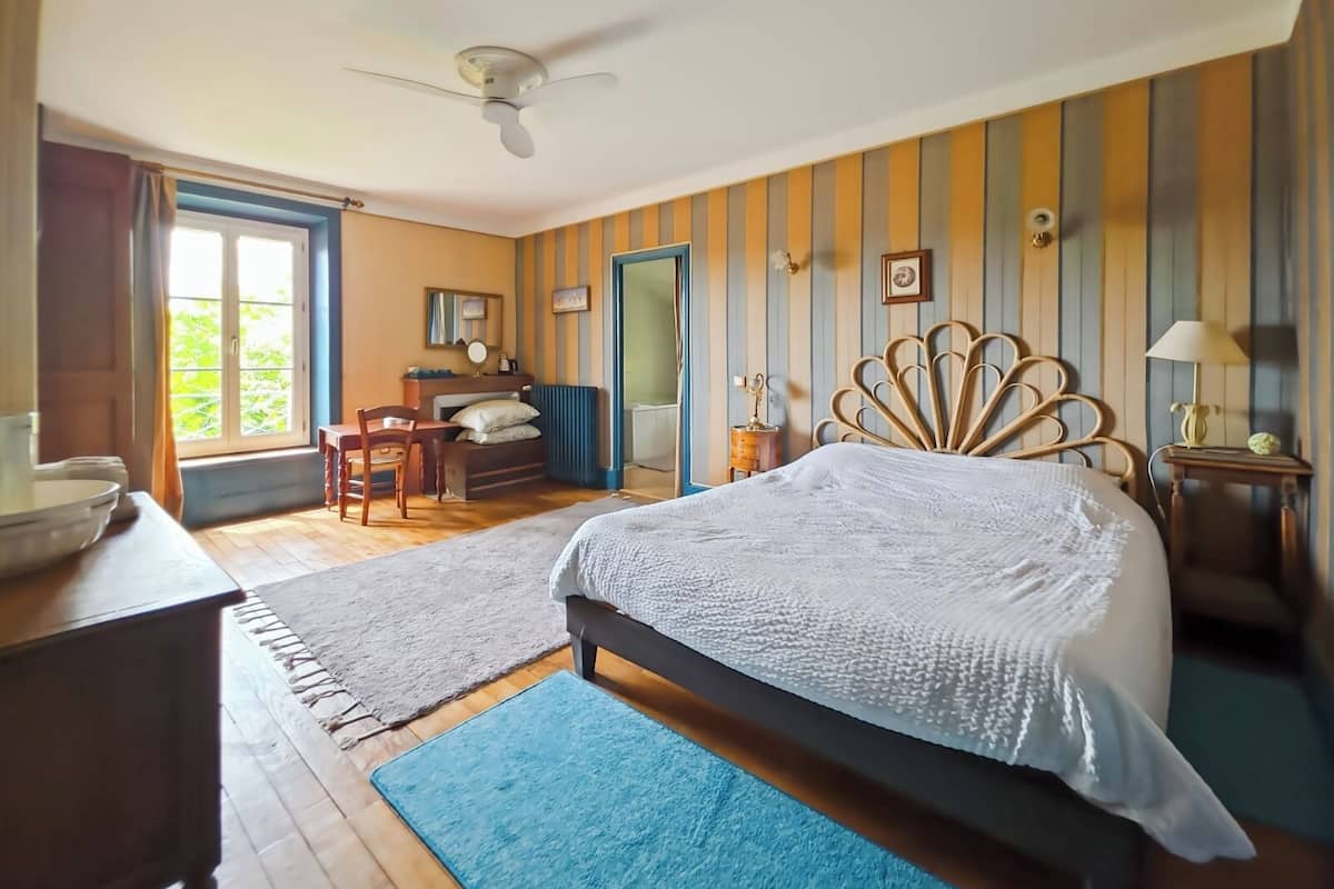 A bedroom with a bed, a desk, a chair, a ceiling fan, and a window with curtains.