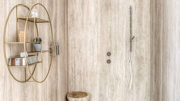 Een badkamer met een marmeren wand, een plank met gouden lijst gevuld met toiletartikelen, een douche met handdouche en een houten kruk.