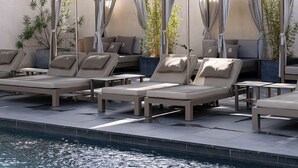 A poolside area with sun loungers and umbrellas, a pool, and a backdrop of trees and a building.