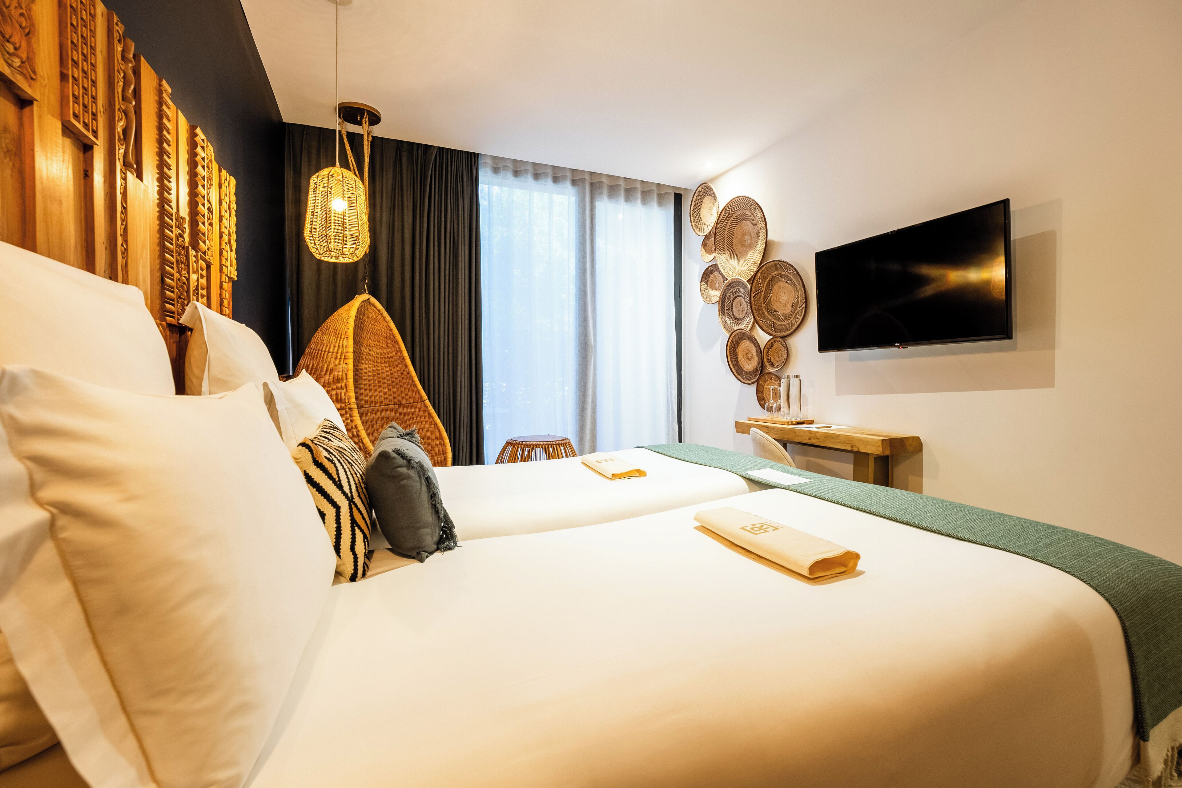 A hotel room with two beds, a flat-screen TV, a woven chair, and a wall with decorative plates.