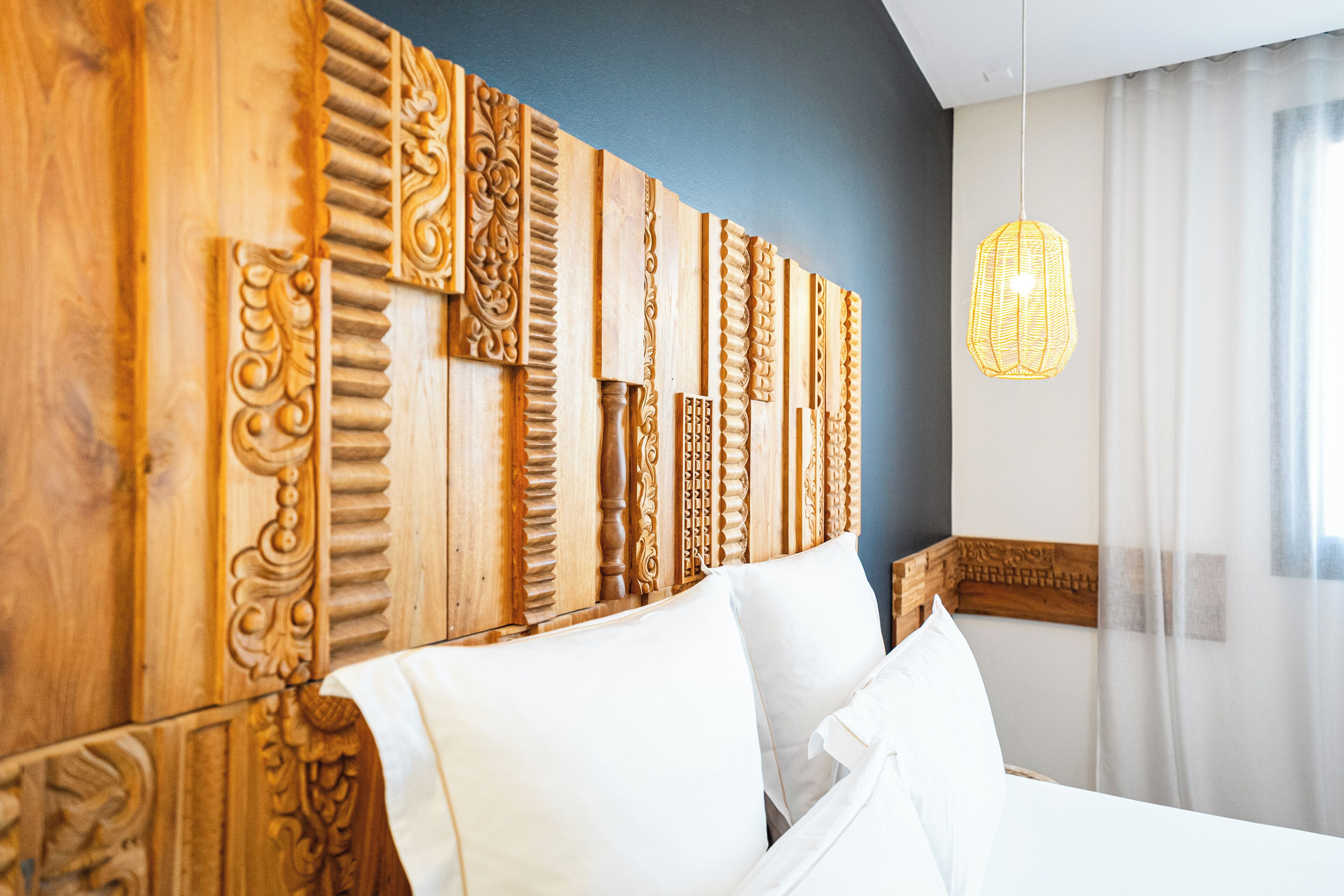 Un dormitorio con cabecera de madera con tallas elaboradas, cama blanca con almohadas y lámpara colgante.