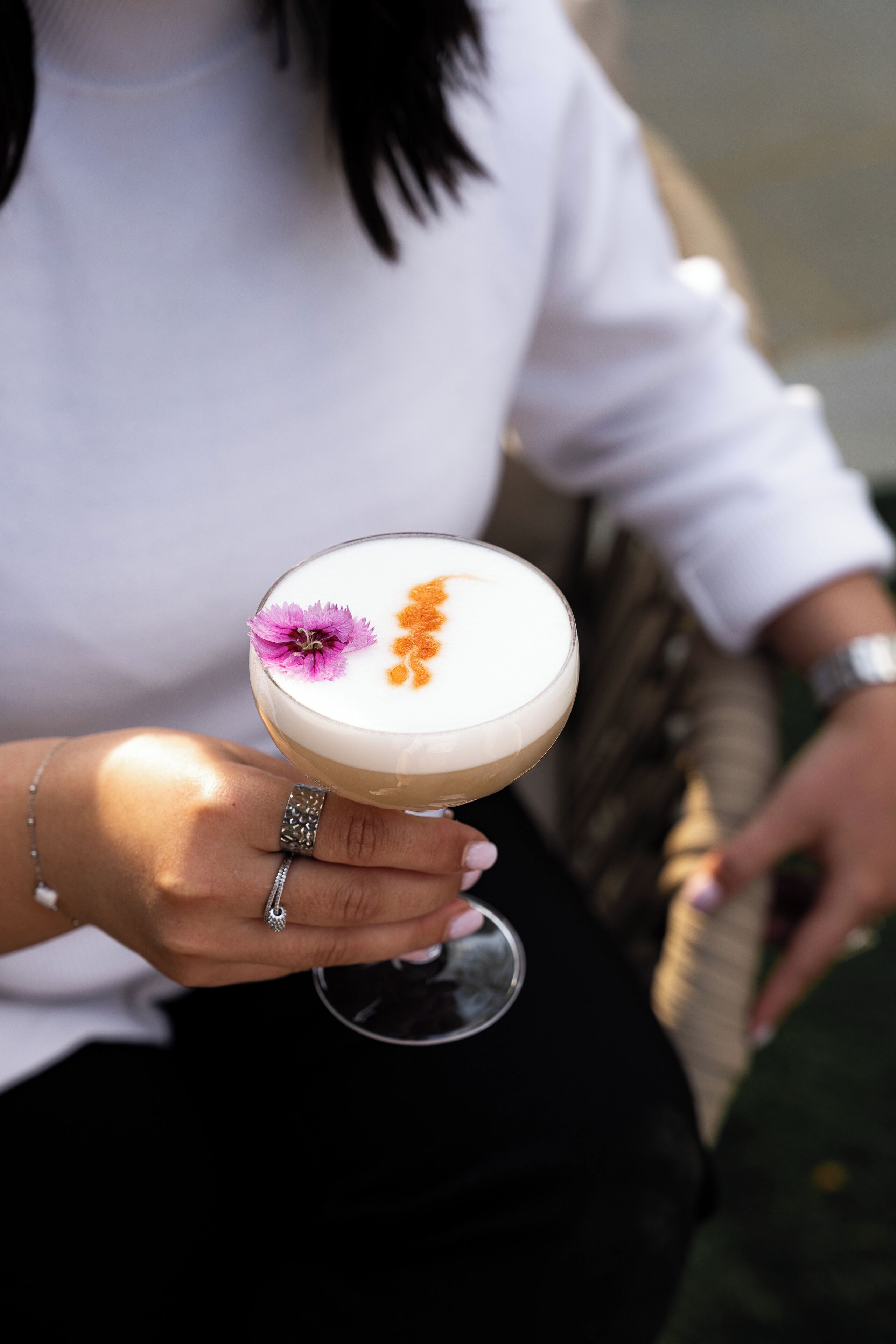 A person holding a cocktail with a flower garnish.