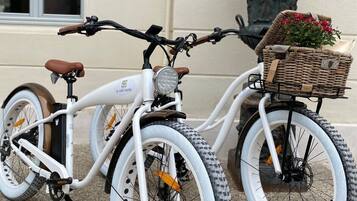 A white bicycle with a basket and a potted plant on the back.