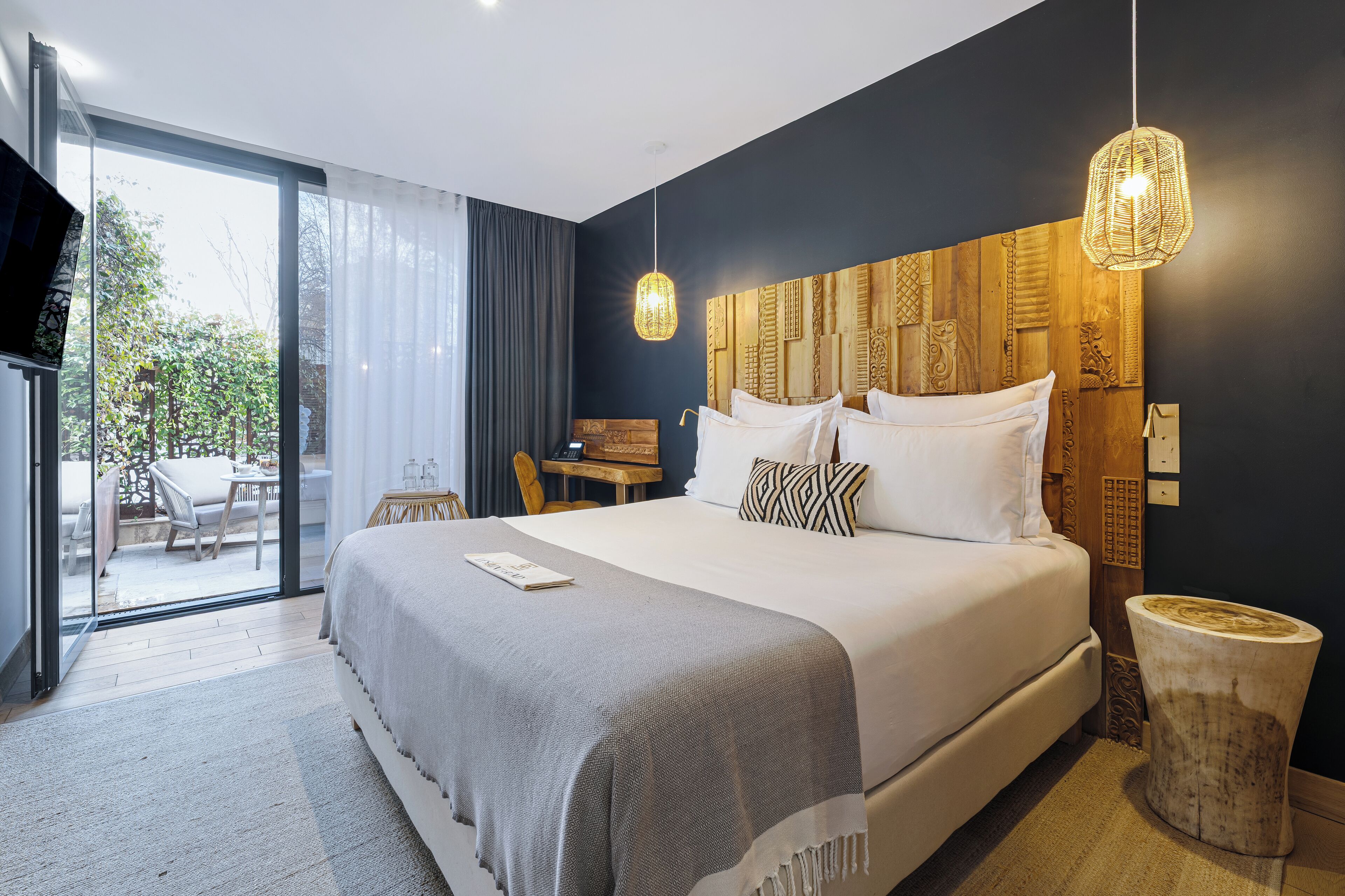 Ett modernt hotellrum med en stor säng, en sänggavel i trä, ett litet bord och utsikt över omgivningarna.
