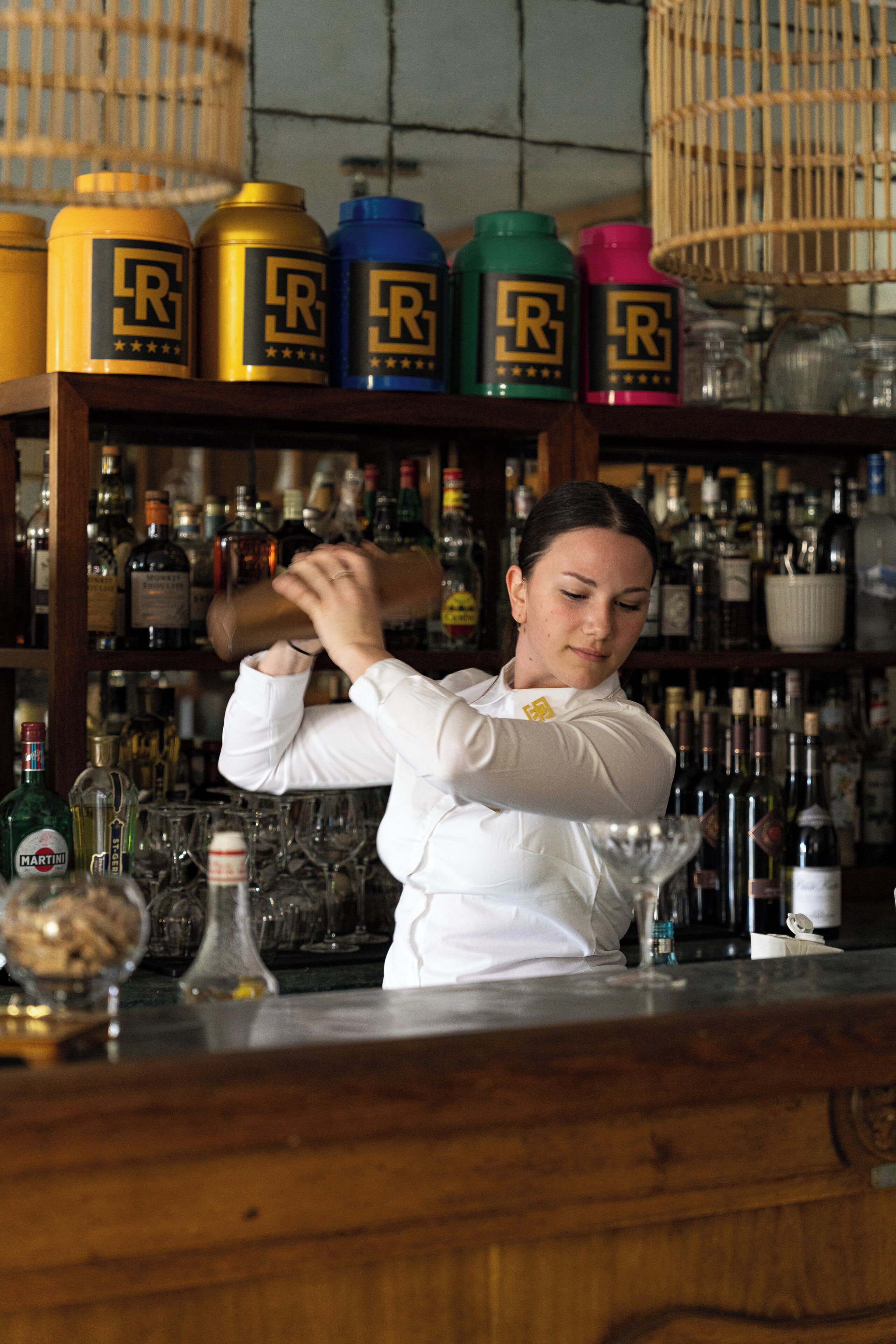 Un bartender preparando una bebida detrás de la barra, con varias botellas y recipientes.