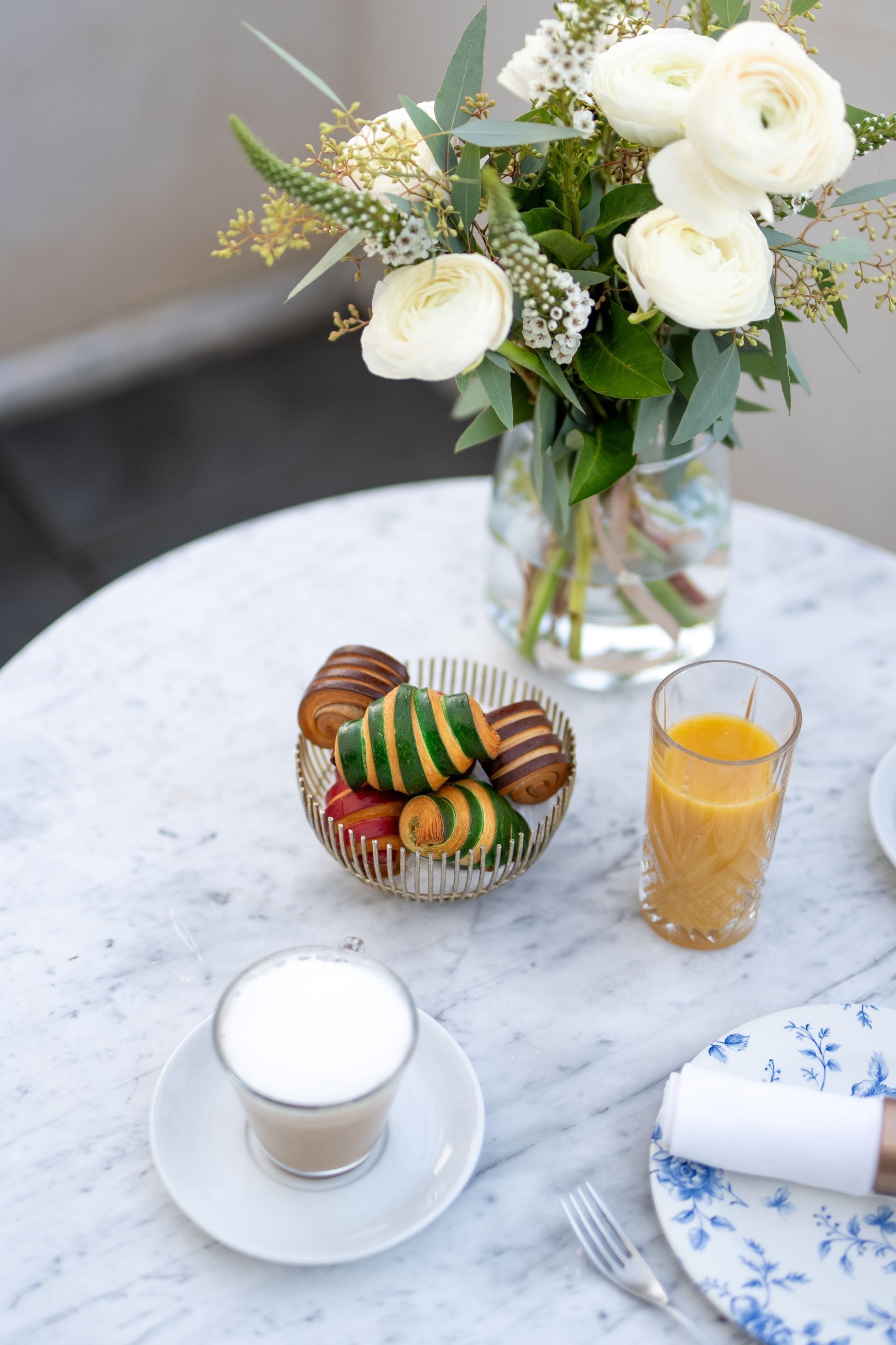 A table with a glass of orange juice, a bowl of cookies, a glass of milk, and a vase with flowers.