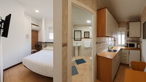 Une chambre de taille réduite comprenant un lit, une petite salle de bain et une kitchenette.