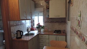 Une cuisine compacte avec des meubles en bois, un évier, une cuisinière et une table à manger sur laquelle sont disposés des fruits.