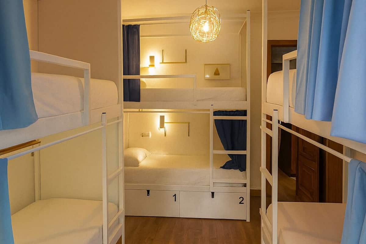 Dormitorio con literas, alfombra a rayas, lámpara colgante y una estantería pequeña con adornos.