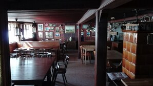 A restaurant with wooden tables and chairs, a bar area with stools, and a wall decorated with framed pictures and hanging plants. - Berggasthaus Kandelhof (Simonswald)