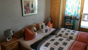 Une chambre à coucher avec un lit en bois, une table de chevet, une lampe, une chaise et une fenêtre avec des rideaux.