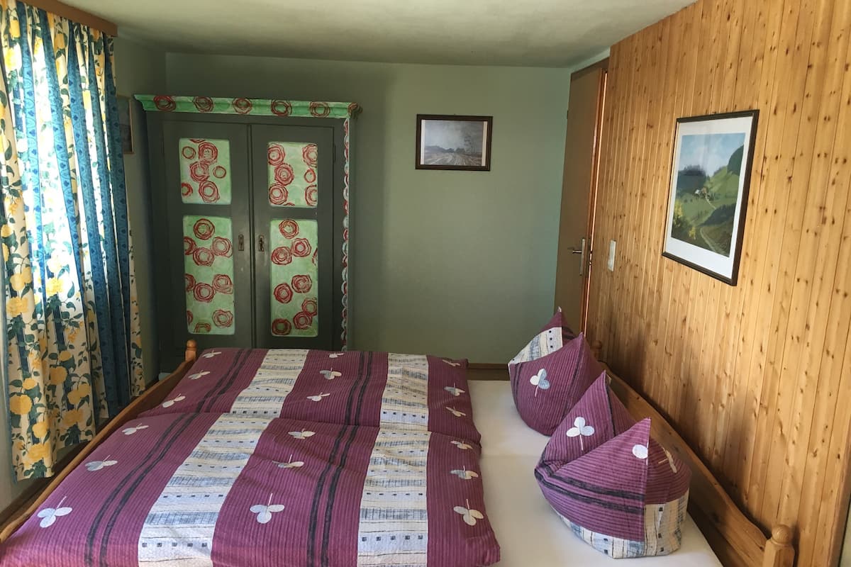 Ein Schlafzimmer mit Bett, Vorhängen, einer Tür mit floralem Muster und zwei gerahmten Bildern an der Wand.