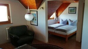 A small, cozy room with a single bed, a green armchair, and a hanging light fixture. - Berggasthaus Kandelhof (Simonswald)