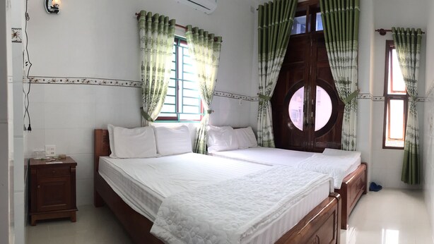A bedroom with a large bed, two windows with curtains, a nightstand, and a wall-mounted air conditioner. - Sunrise Guesthouse (Quy Nhon Nam)