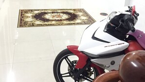 A room with a tiled floor, a patterned rug, a white scooter, and a wooden cabinet. - Sunrise Guesthouse (Quy Nhon Nam)