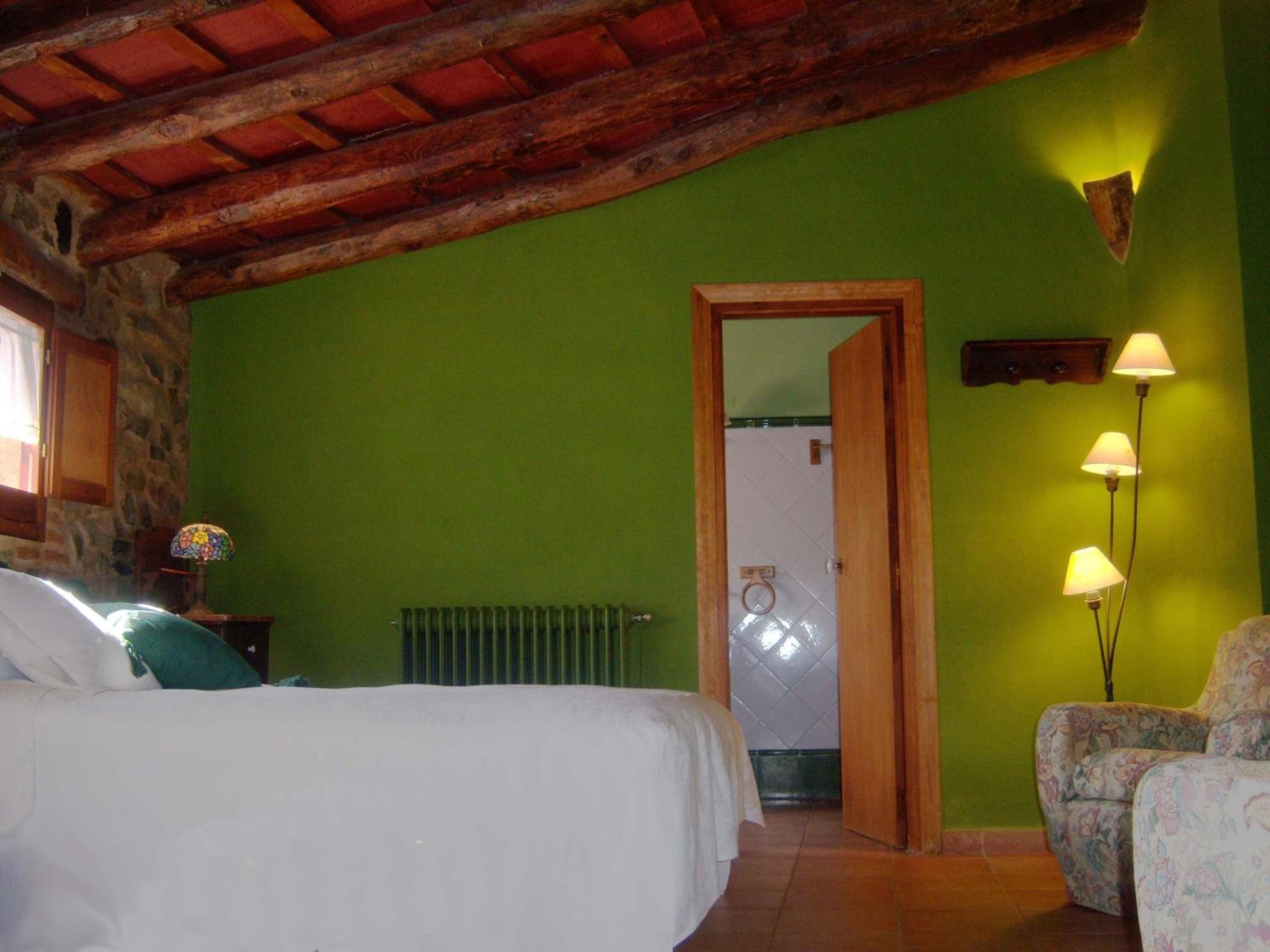 A bedroom with a bed, a chair, a lamp, and a door leading to a bathroom.