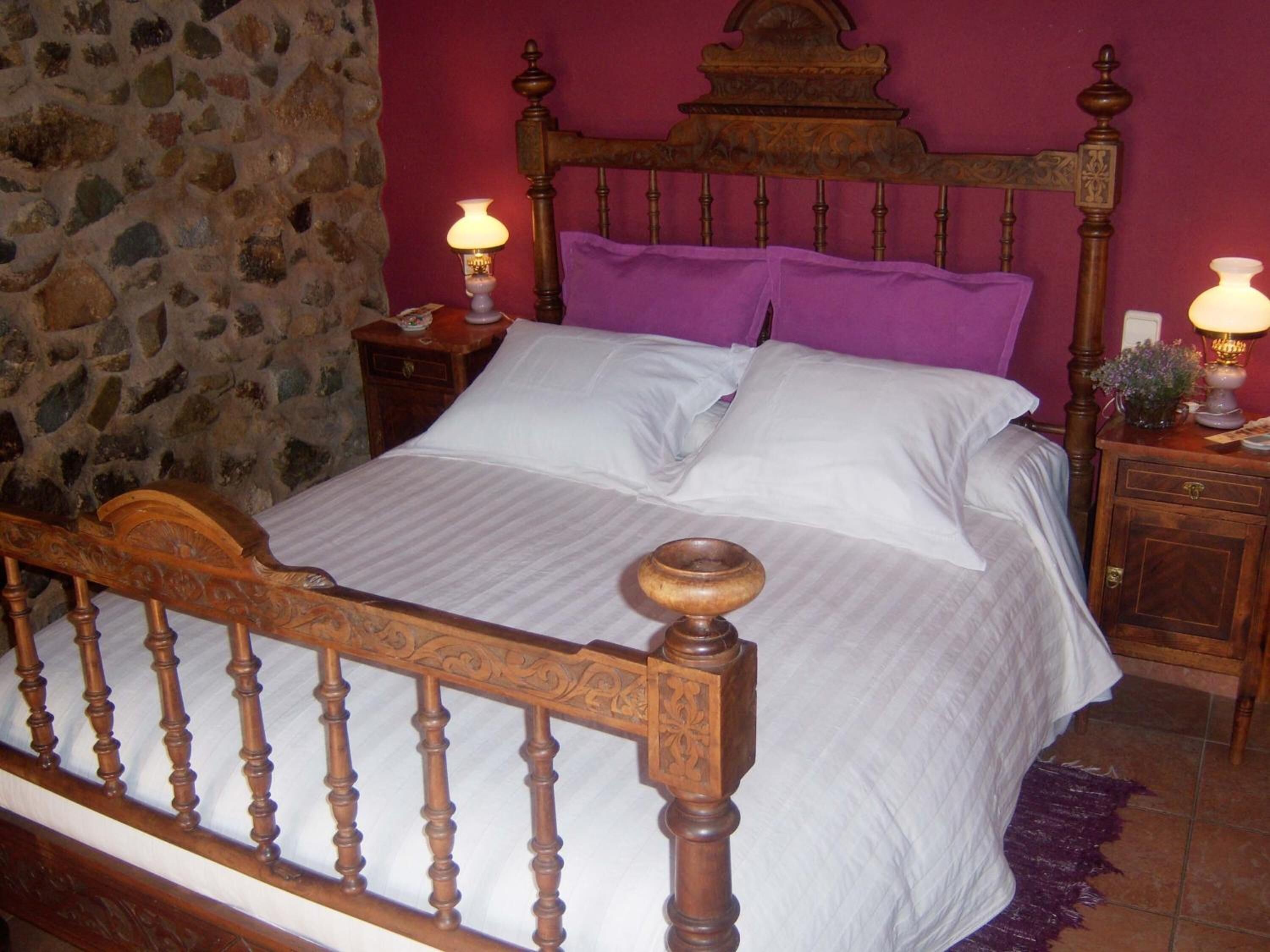 A bed with a wooden headboard, a stone wall, and a purple pillow.