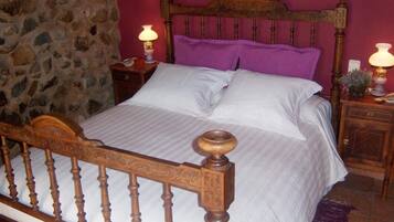 A bed with a wooden headboard, a stone wall, and a purple pillow.