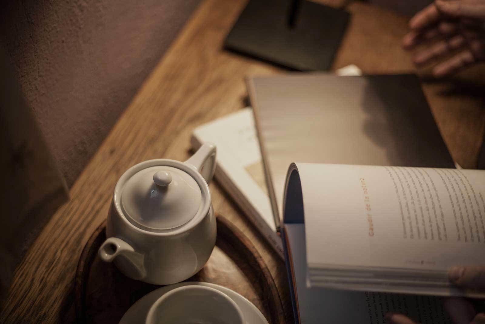 A wooden table with a teapot, a cup, and an open book.