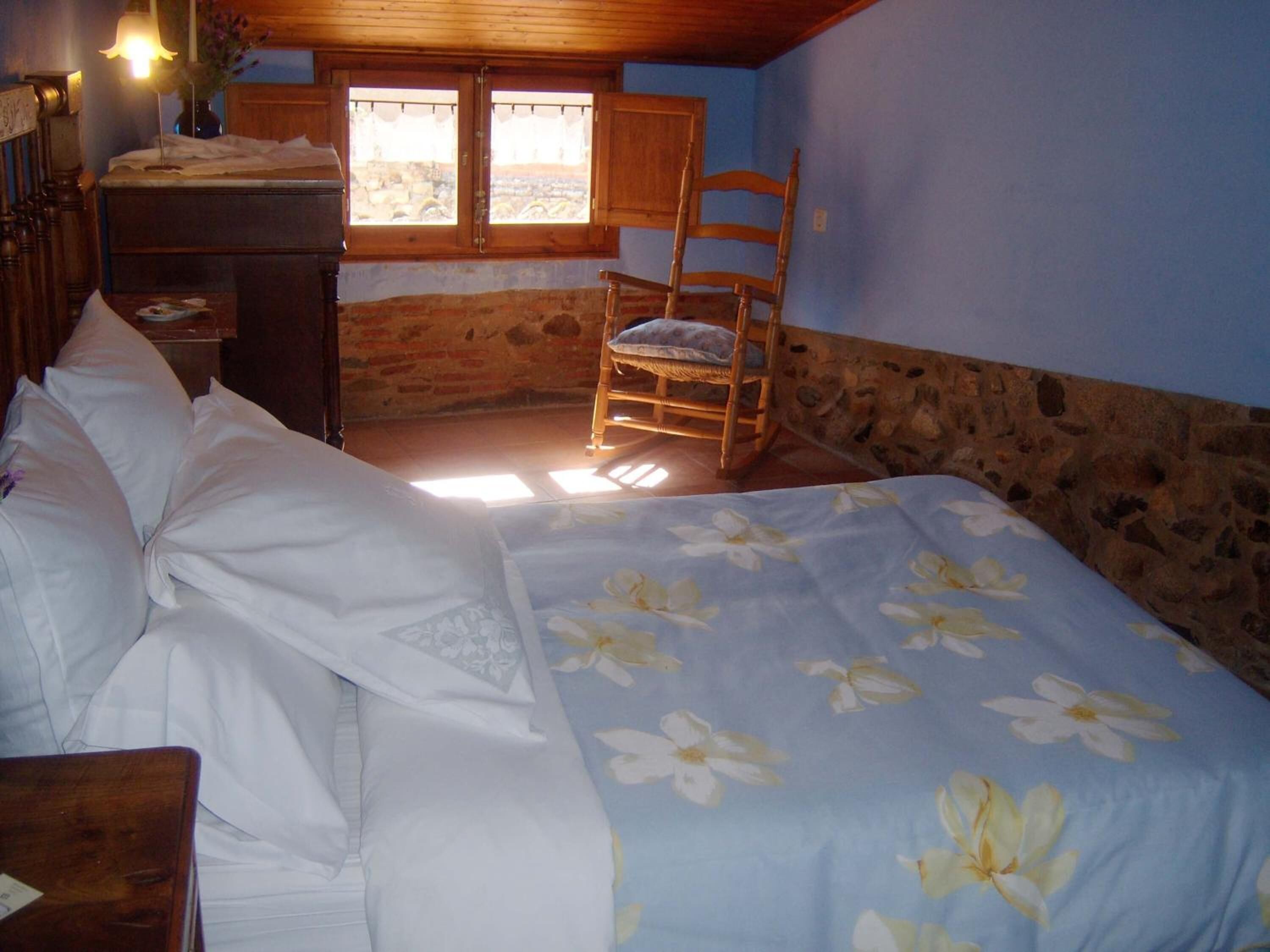 Un dormitorio con cama, una silla de madera y una ventana con vistas.
