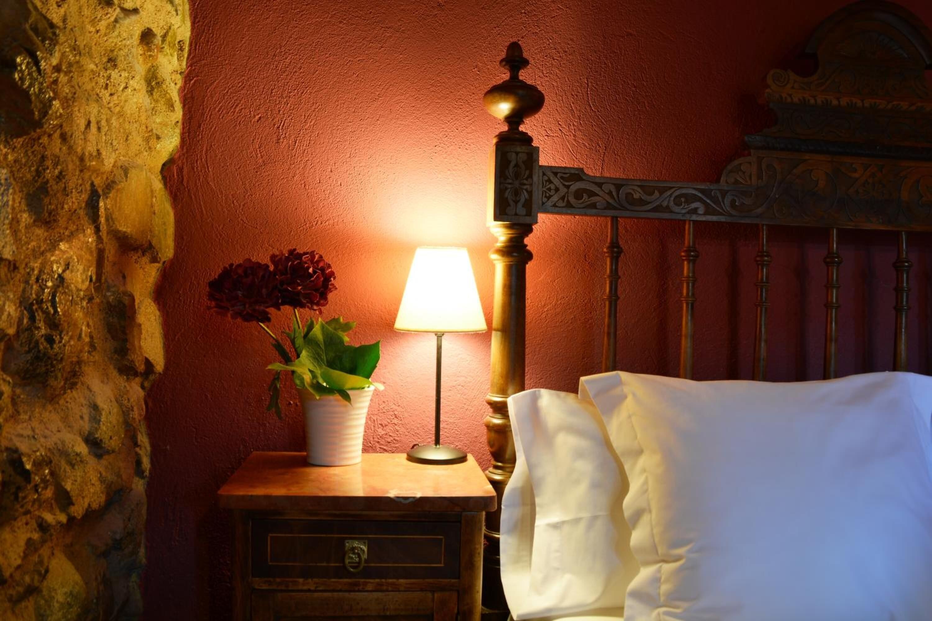 Een houten nachtkastje met een lamp, een potplant en een wit kussen op een bed met hoofdeinde.