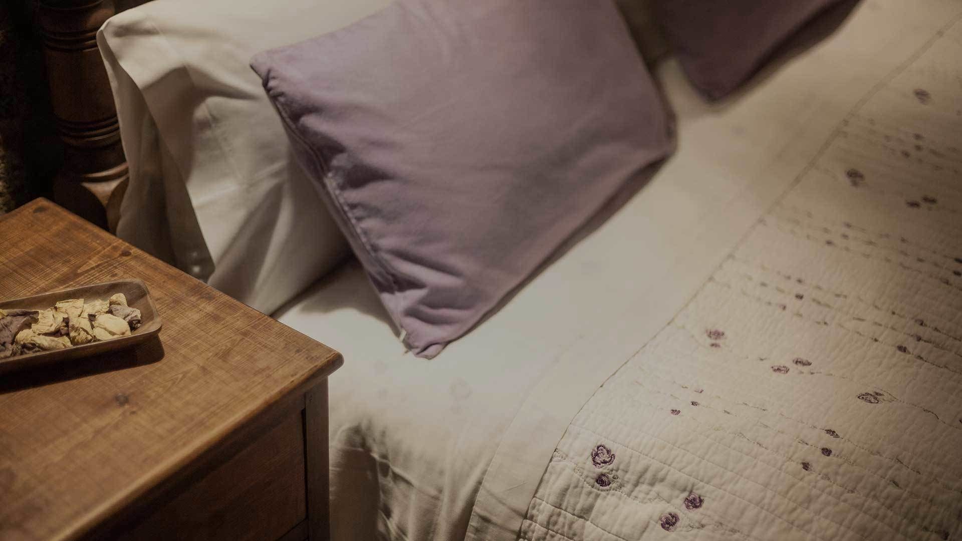 A bed with a floral-patterned bedspread and two pillows, one purple and one white.
