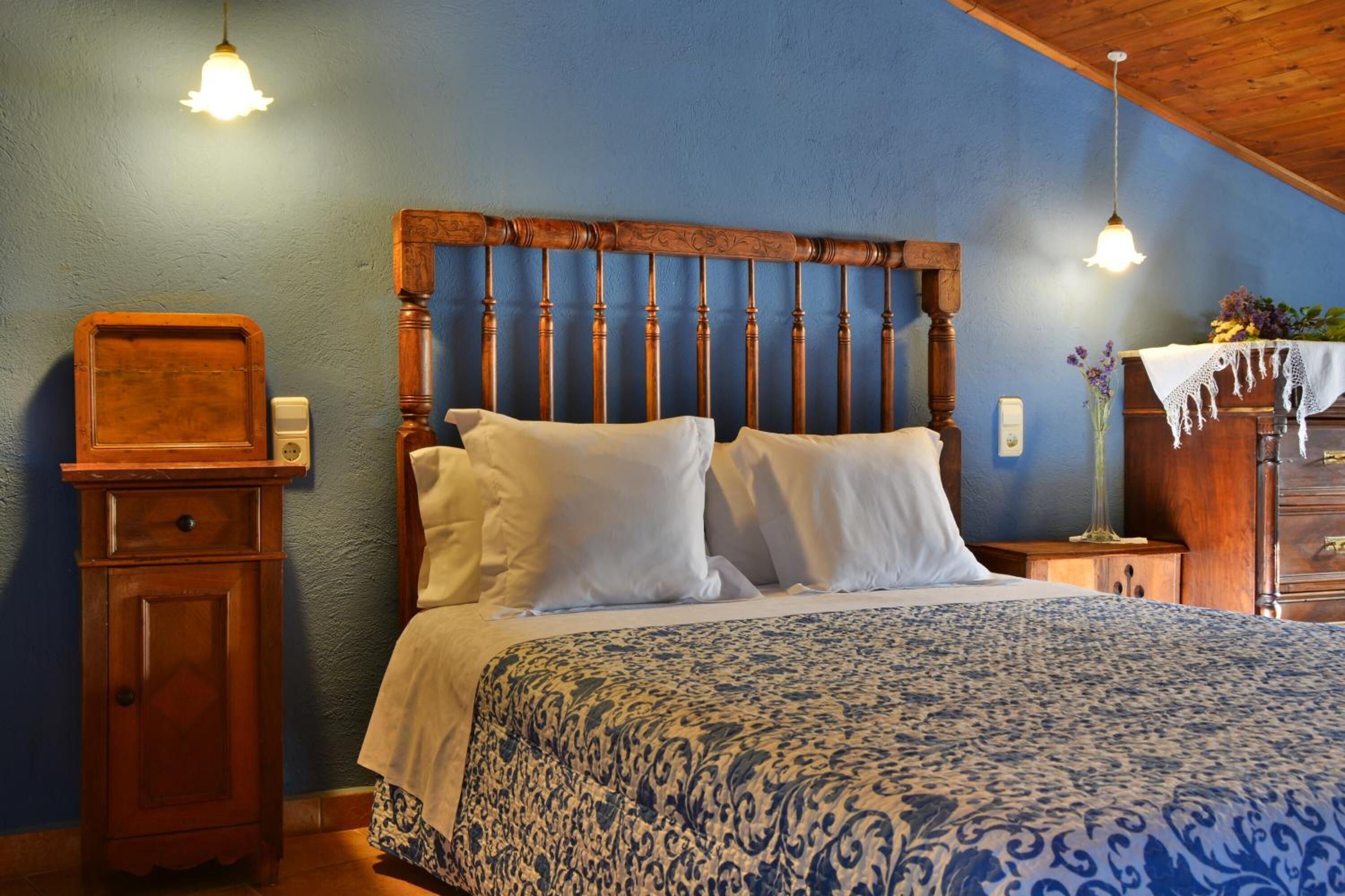 Een slaapkamer met een houten hoofdeinde, een bed met witte lakens, een nachtkastje, een houten dressoir en twee hangende lampen.