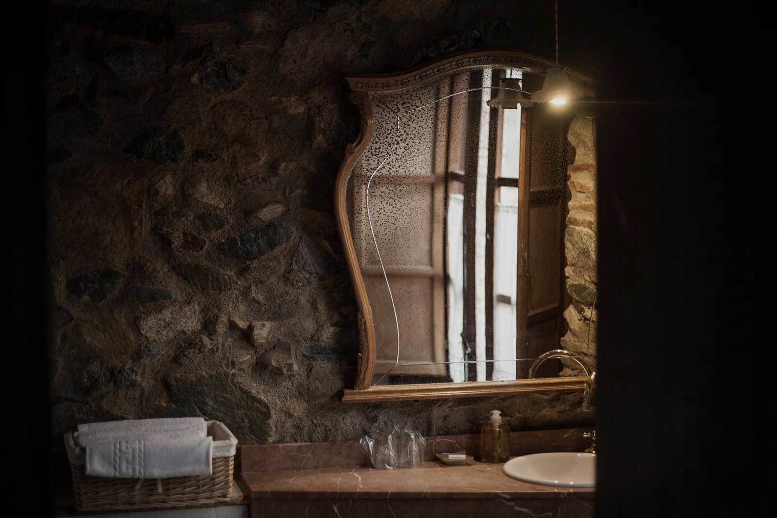 Un baño rústico con pared de piedra, tocador de madera, espejo y toalla en una cesta.