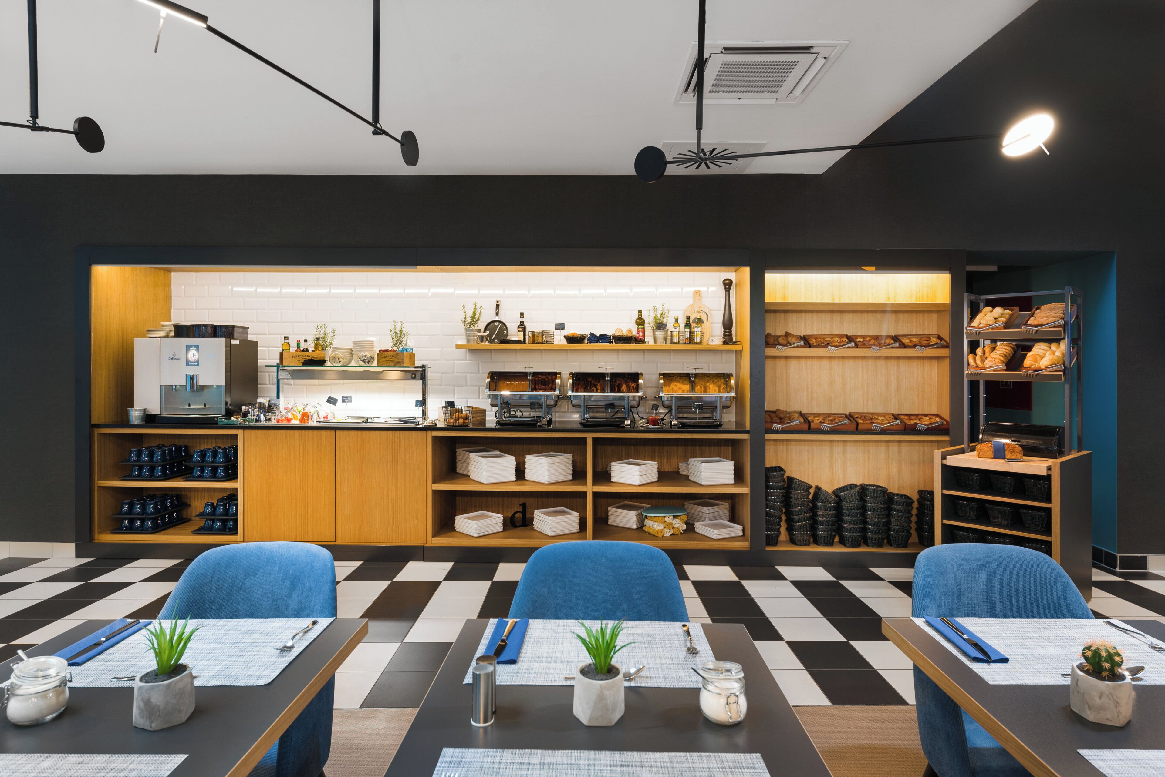 A modern cafe with checkered flooring, blue chairs, a counter with various items, and shelves with baked goods.