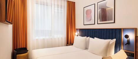 Habitación de hotel con una cama grande, una mesita de noche, un televisor montado en la pared y dos cuadros enmarcados.