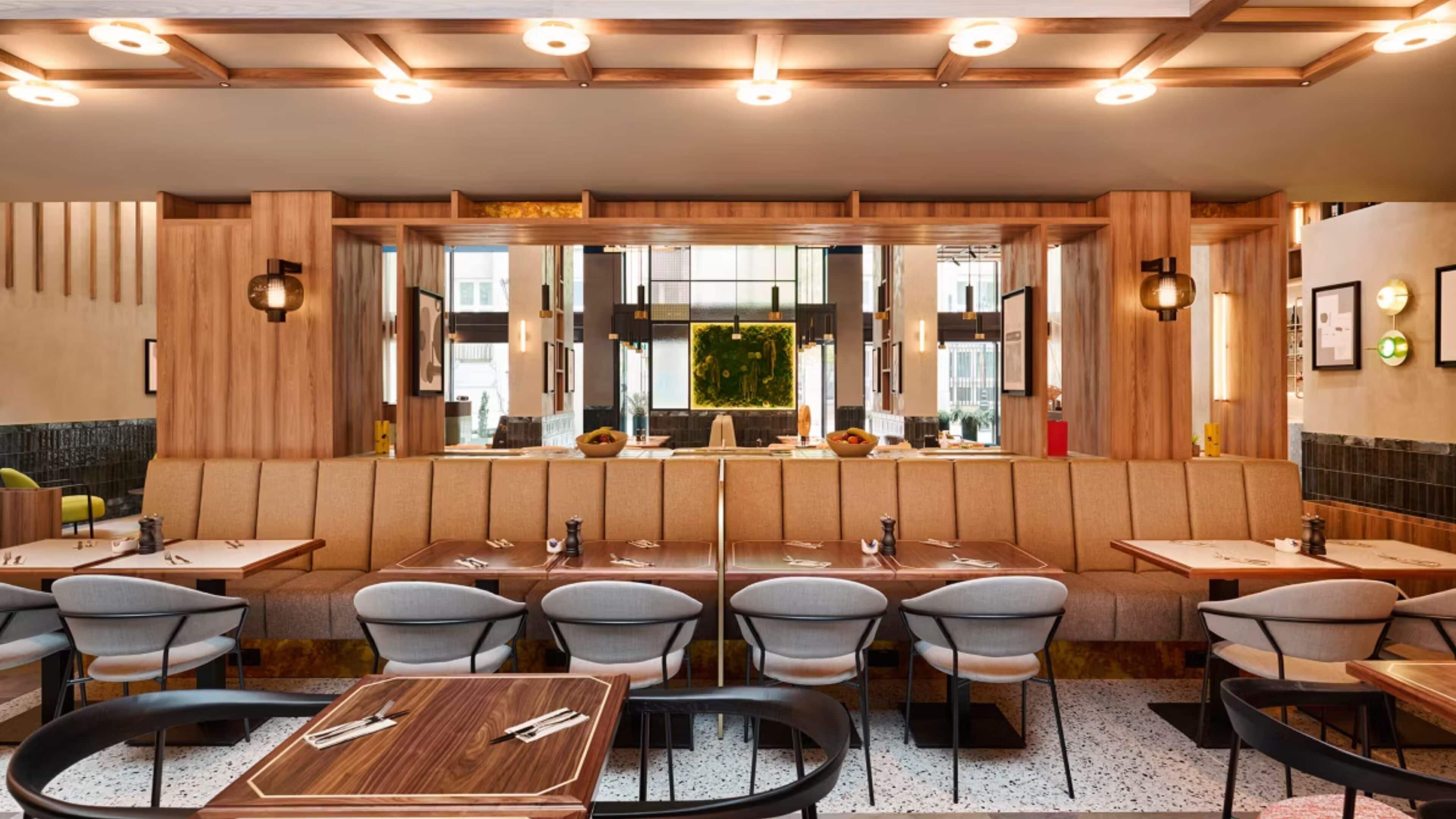 Ein Restaurant mit Sitzecken, Tischen und Stühlen, Holzvertäfelung und Pendelleuchten.