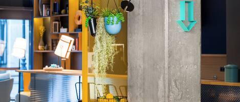 A modern interior with a concrete pillar, hanging plants, a yellow bookshelf, and a directional sign.