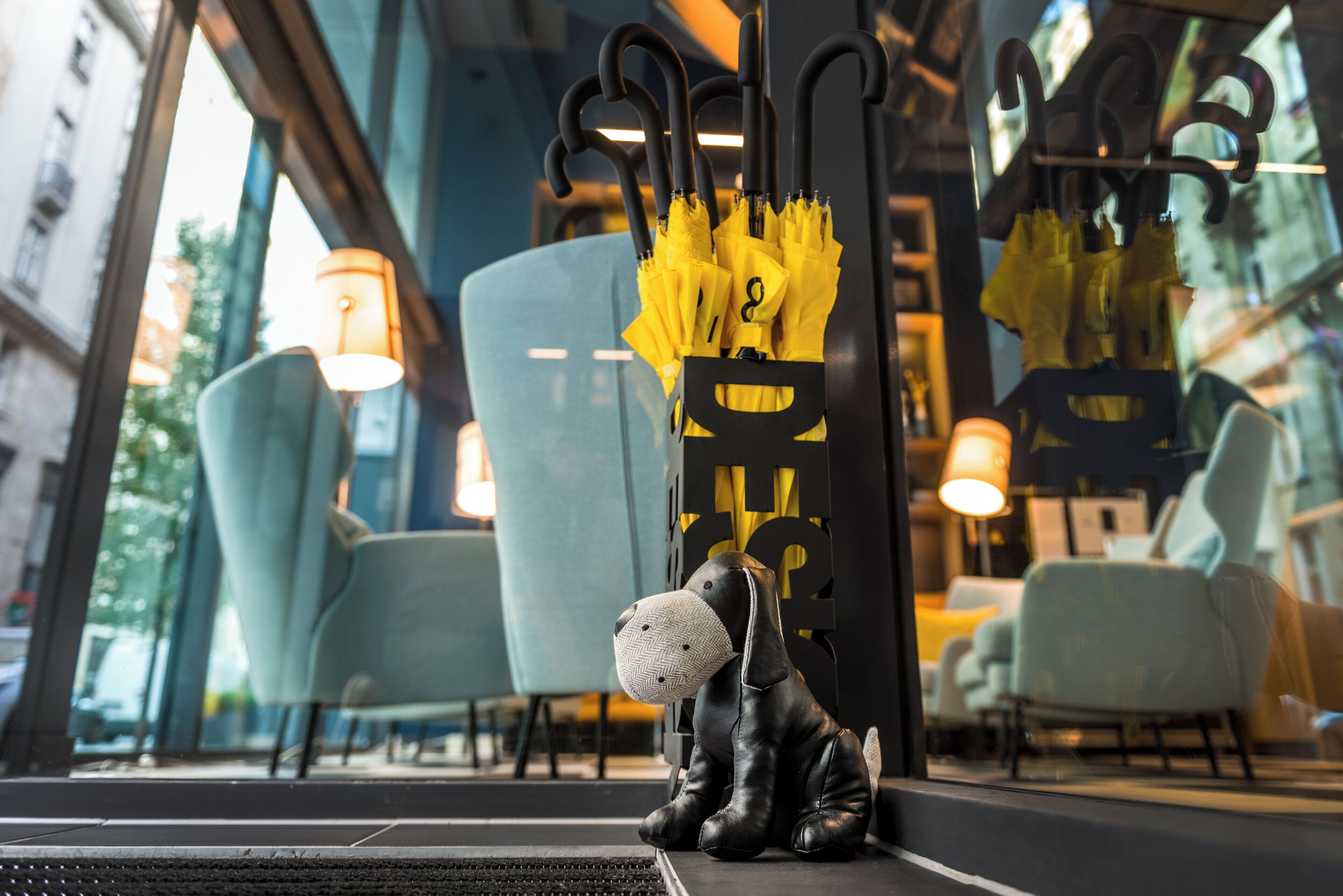 Una estatua de perro negro, un paraguas amarillo y una silla azul en un interior moderno.