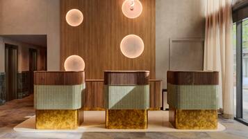 Zona de recepción con tres mostradores, un muro de madera y luces circulares en la pared.