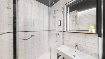 Un baño moderno con azulejos blancos, una cabina de ducha de vidrio, un lavamanos con espejo y un perchero para toallas.